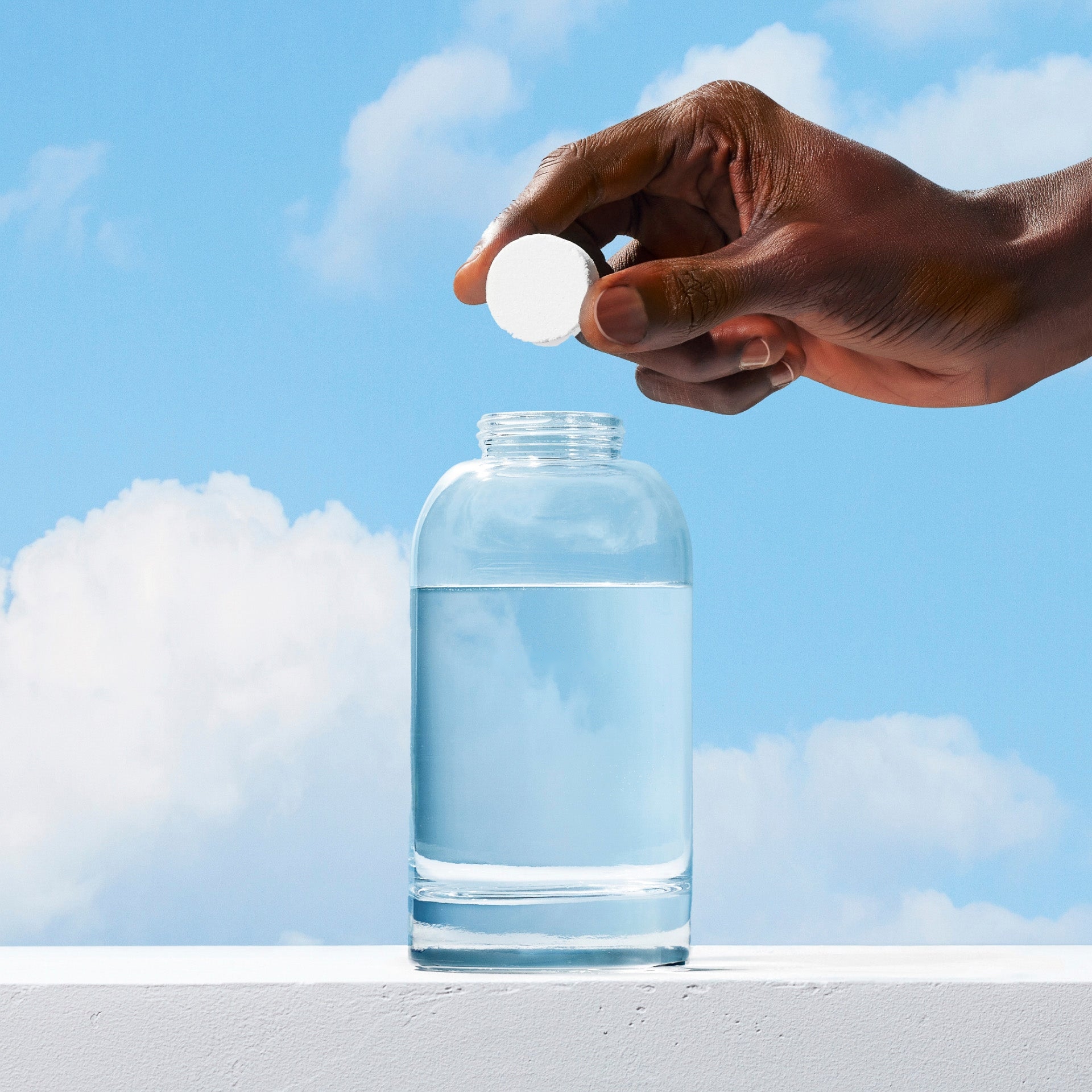 A laundry tablet held over a glass bottle of water